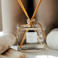 Clear glass diffuser bottle with wooden sticks on a neutral background